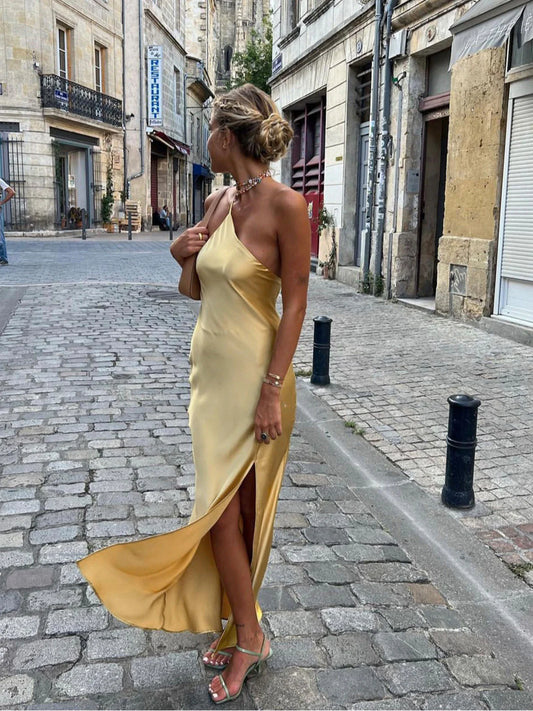 Model draagt een goudkleurige, satijnen maxi-jurk met open rug en blote schouders in Parijs – perfecte jurk voor feest of zomerse avond.